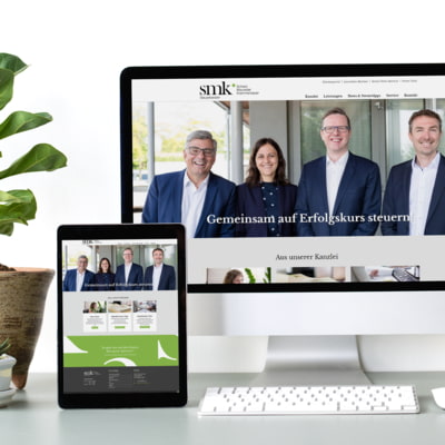 Handy, Laptop und Desktop mit geöffneter Website der Firma SMK, daneben grüne Pflanze