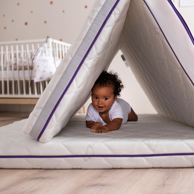 Baby unter aufgestellter Babymatratze mit Gitterbett im Hintergrund