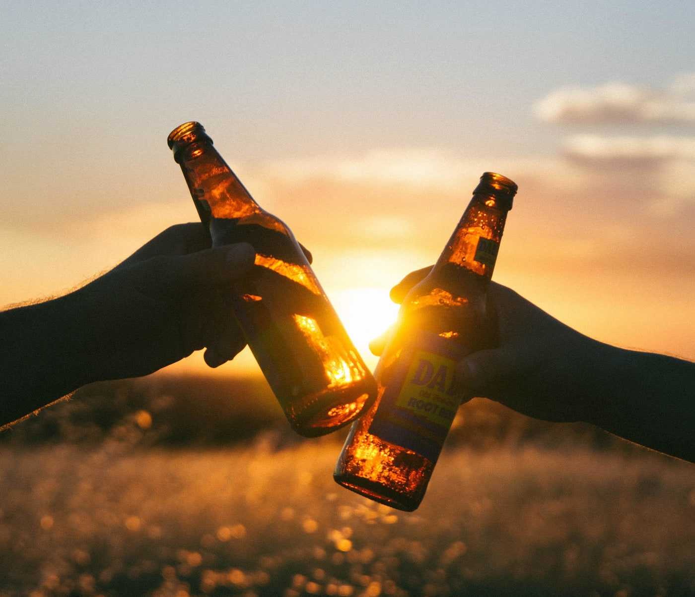 Zwei Personen die bei Sonnenuntergang mit Bierflaschen anstoßen