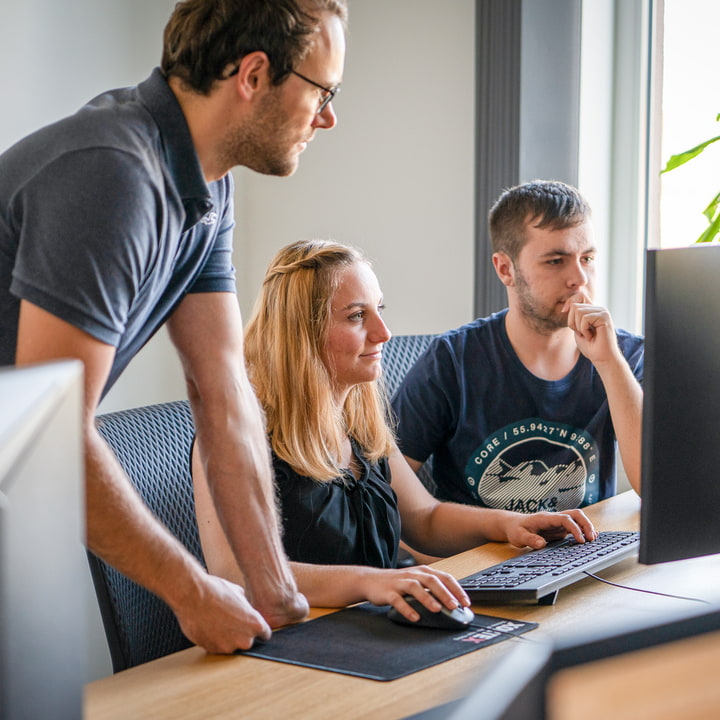 XORTEX Team Drei Personen sitzen am Schreibtisch und arbeiten gemeinsam auf einem Bildschirm.