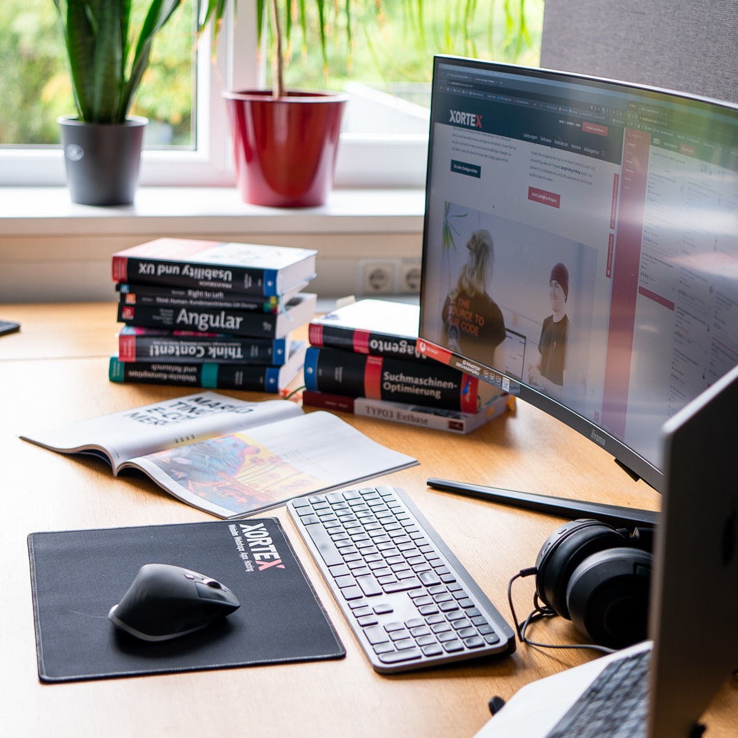 Arbeitsplatz mit Maus, Tastatur, Bildschirm, Laptop und Fachliteratur