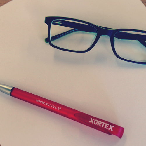 Brille und XORTEX Stift auf einem Blatt Papier