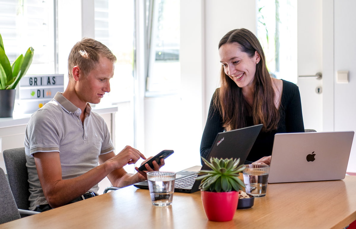 Ein Mann und eine Frau sitzen in einem Besprechungsraum an einem Tisch mit jeweils einem Laptop. Ein Mann und eine Frau sitzen in einem Besprechungsraum an einem Tisch mit jeweils einem Laptop.