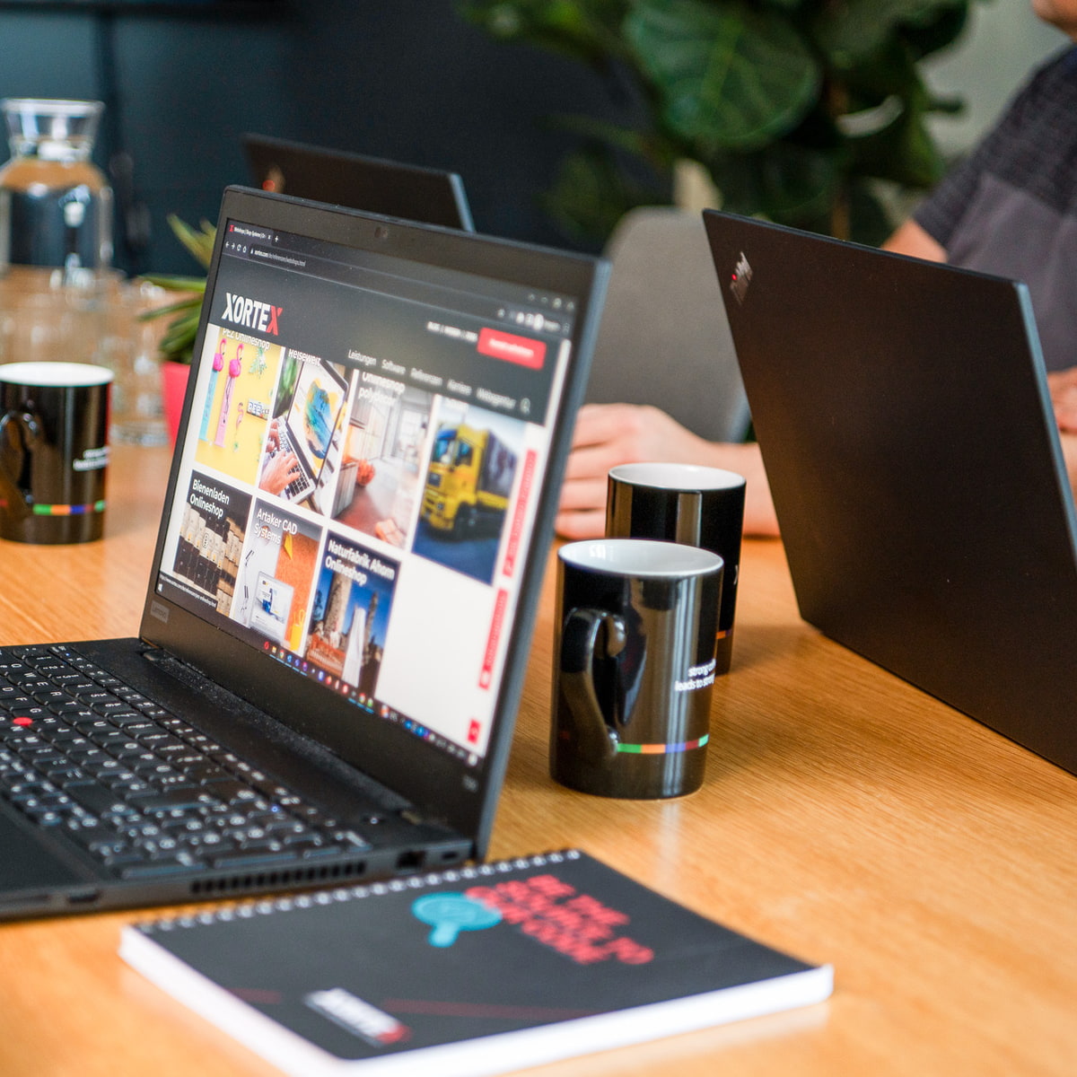 XORTEX eBusiness GmbH Laptops mit Referenzen, Notizblock und Kaffeetassen