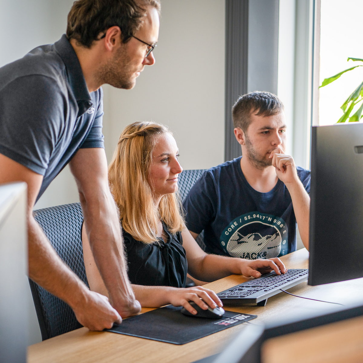 Drei Personen sitzen am Schreibtisch und arbeiten gemeinsam auf einem Bildschirm. Drei Personen sitzen am Schreibtisch und arbeiten gemeinsam auf einem Bildschirm.